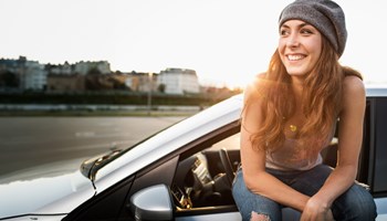 Jeune femme heureuse avec sa voiture assurée chez AXA.