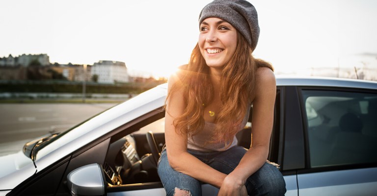 Jeune femme heureuse avec sa voiture assurée chez AXA.