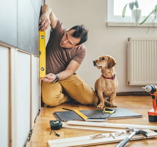 Man renoveert zijn huis met zijn hond naast hem.