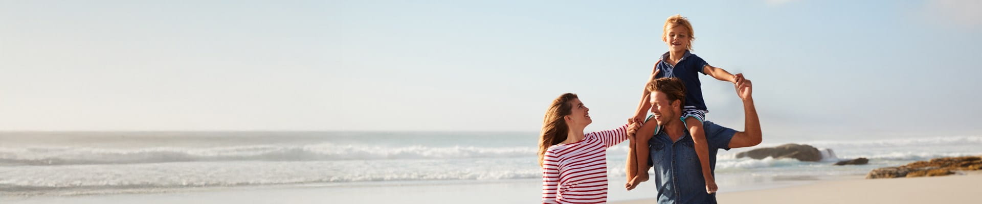 Ouders en hun kind genieten volop van een strandwandeling dankzij de AXA Reisverzekering.