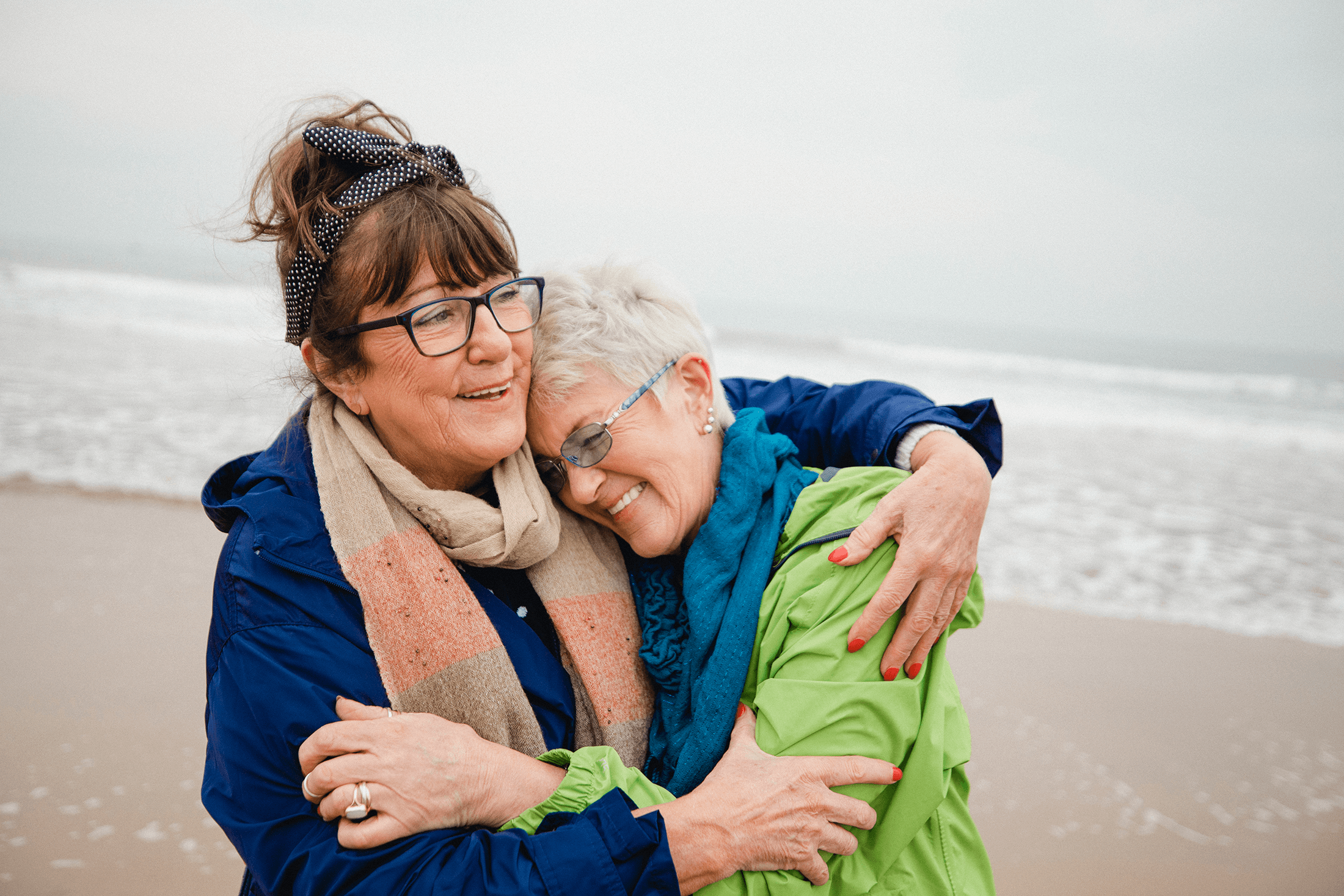 Deux amies s’enlacent sur la plage. Elles profitent à un âge avancé du rendement supplémentaire que leur assurance investissement leur a apporté. 