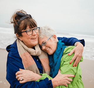 Deux amies s’enlacent sur la plage. Elles profitent à un âge avancé du rendement supplémentaire que leur assurance investissement leur a apporté.