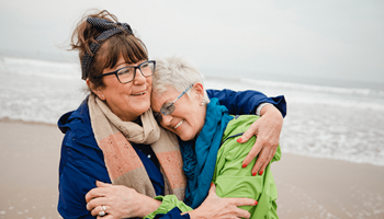 Twee vriendinnen omhelzen elkaar op het strand. Ze genieten op hun oude dag van het extra rendement dat hun beleggingsverzekering hen heeft opgebracht.