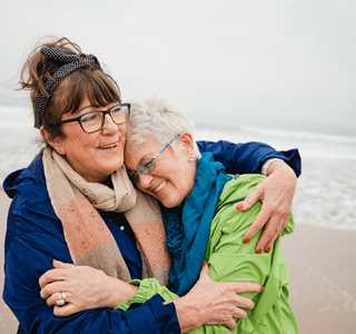 Twee vriendinnen omhelzen elkaar op het strand. Ze genieten op hun oude dag van het extra rendement dat hun beleggingsverzekering hen heeft opgebracht.