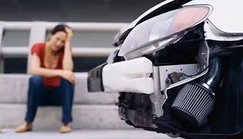 Vrouw zittend naast haar beschadigde auto na een ongeluk.