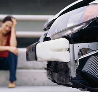 Vrouw zittend naast haar beschadigde auto na een ongeluk.