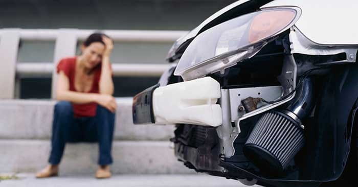 Vrouw zittend naast haar beschadigde auto na een ongeluk.