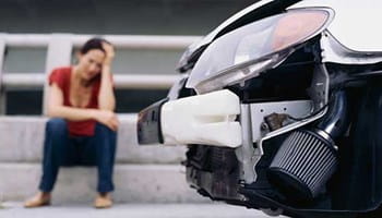Femme assise à côté de sa voiture endommagée à la suite d’un accident.