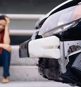 Femme assise à côté de sa voiture endommagée à la suite d’un accident.