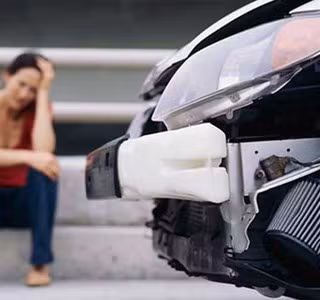 Femme assise à côté de sa voiture endommagée à la suite d’un accident.