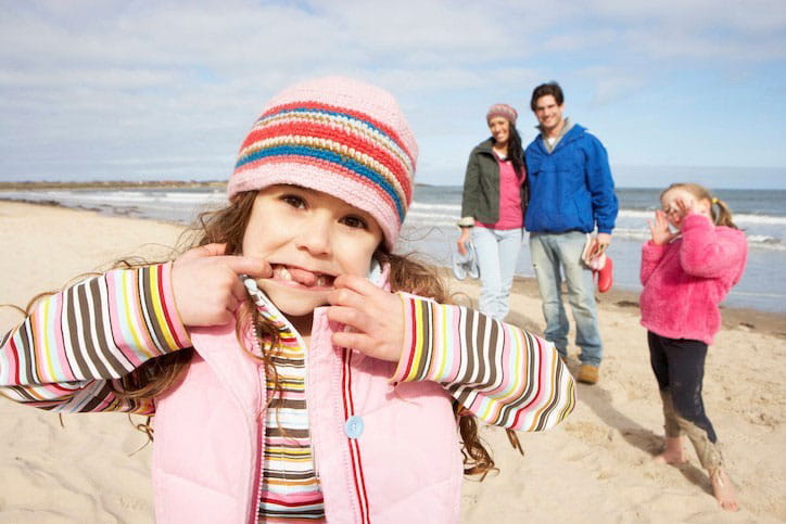 Een gezin met twee kinderen geniet van een zorgeloze strandwandeling dankzij de bescherming van hun familiale en ongevallenverzekering. 