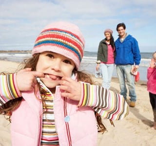 Een gezin met twee kinderen geniet van een zorgeloze strandwandeling dankzij de bescherming van hun familiale en ongevallenverzekering.
