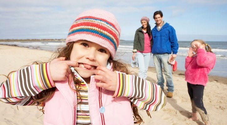 Een gezin met twee kinderen geniet van een zorgeloze strandwandeling dankzij de bescherming van hun familiale en ongevallenverzekering.