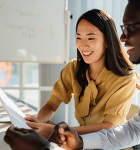 Deux collègues consultant ensemble un document devant un ordinateur portable, illustrant une situation professionnelle liée à la continuité d’activité d’un dirigeant ou indépendant immobilisé temporairement.