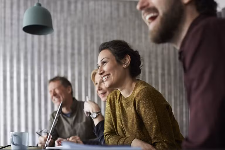 Vrolijke en creatieve collega's zitten rond een vergadertafel en kijken voor zich uit in een vergaderzaal.
