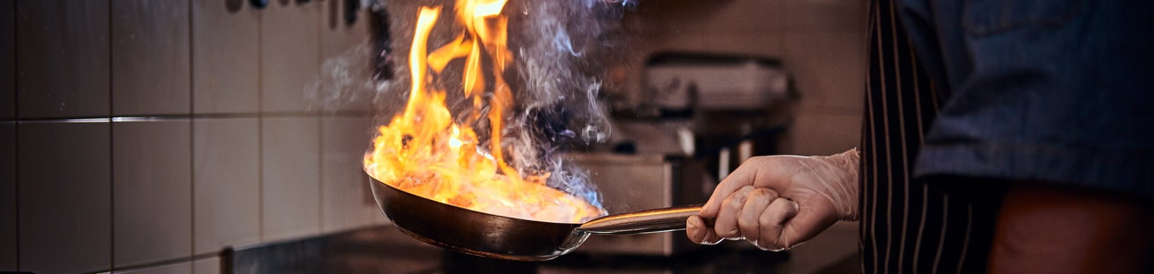 Persoon heeft tijdens het koken een vlam in de pan, wat een belangrijke oorzaak is van woningbranden.