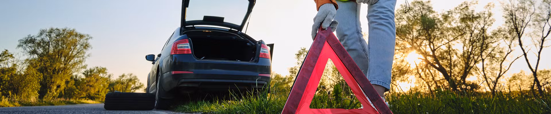 Vrouw vervangt een autowiel na een ongeval en plaatst de gevarendriehoek.