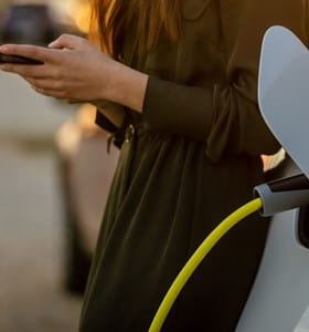Une femme regarde son smartphone pendant que sa voiture électrique se recharge
