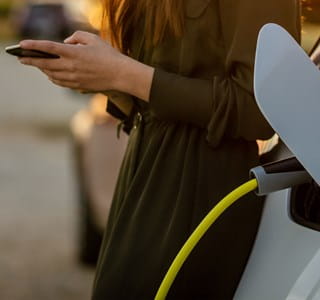 Une femme regarde son smartphone pendant que sa voiture électrique se recharge