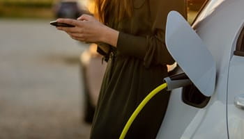 Vrouw die op haar smartphone kijkt terwijl haar elektrische auto oplaadt