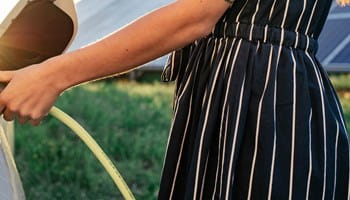 Vrouw die haar elektrische auto oplaadt op een zomerse dag.