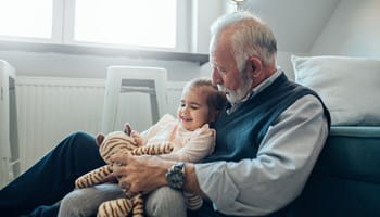 Grand-père qui a désigné sa petite-fille comme bénéficiaire dans un contrat d'assurance-vie et qui joue avec elle et sa peluche dans le séjour.