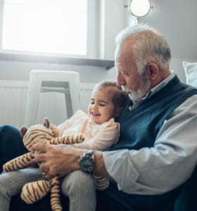 Grand-père qui a désigné sa petite-fille comme bénéficiaire dans un contrat d'assurance-vie et qui joue avec elle et sa peluche dans le séjour.
