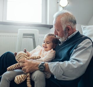 Grand-père qui a désigné sa petite-fille comme bénéficiaire dans un contrat d'assurance-vie et qui joue avec elle et sa peluche dans le séjour.