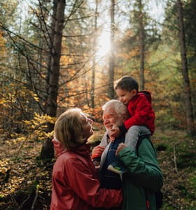 Grootvader, dochter en kleindochter wandelen in het bos en voeren een gesprek over de levensverzekering als successieplanningsinstrument.