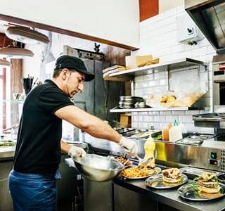 Un membre du personnel de l'horeca prépare et sert des plats selon les directives d'AFSCA et HACCP.