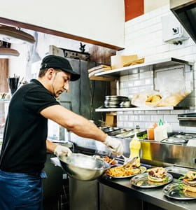 Een horecapersoneelslid bereidt en serveert gerechten volgens de FAVV- en HACCP-richtlijnen.