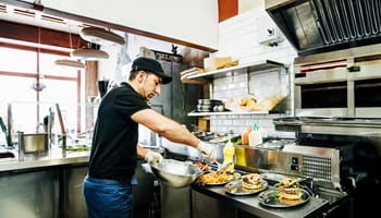Een horecapersoneelslid bereidt en serveert gerechten volgens de FAVV- en HACCP-richtlijnen.
