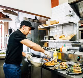 Een horecapersoneelslid bereidt en serveert gerechten volgens de FAVV- en HACCP-richtlijnen.