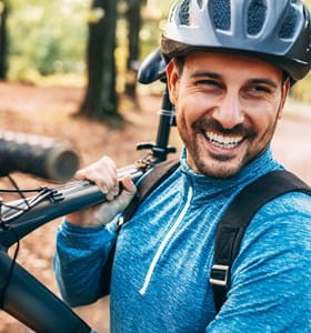 Man met fietshelm lacht omdat hij een autoverzekering per kilometer heeft.