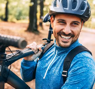Man met fietshelm lacht omdat hij een autoverzekering per kilometer heeft.