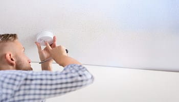 Een huiseigenaar controleert of zijn rookmelder goed werkt.