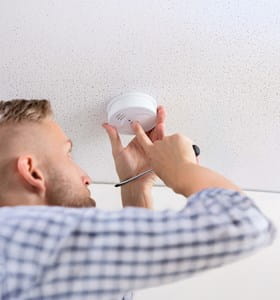 Een huiseigenaar controleert of zijn rookmelder goed werkt.