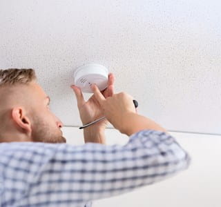 Een huiseigenaar controleert of zijn rookmelder goed werkt.