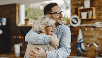 Une mère souriante enlace son fils dans la cuisine après avoir discuté d’investissement en cycle de vie en branche 23 à la table.