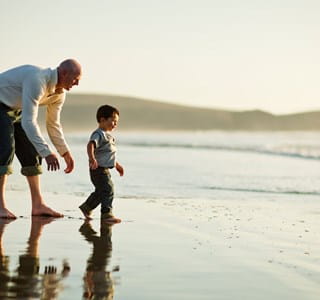 Un homme accompagné d’un enfant, se promenant au bord de plage et ayant l’esprit tranquille grâce à l’assurance voyage souscrite en Belgique.