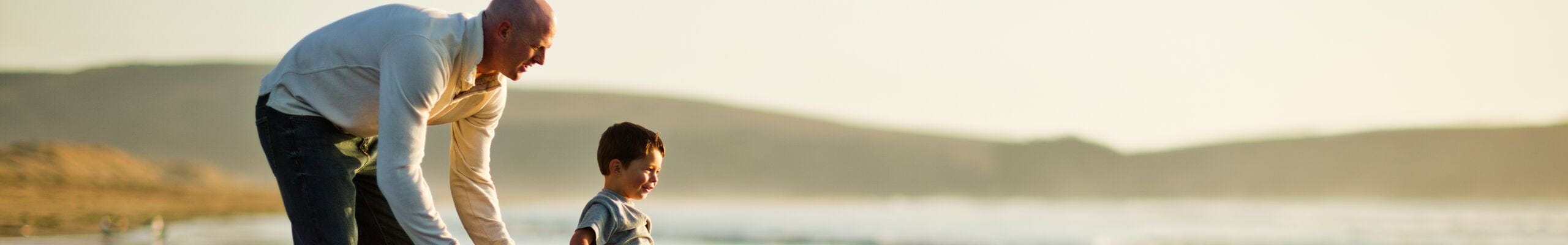 Un homme accompagné d’un enfant, se promenant au bord de plage et ayant l’esprit tranquille grâce à l’assurance voyage souscrite en Belgique.