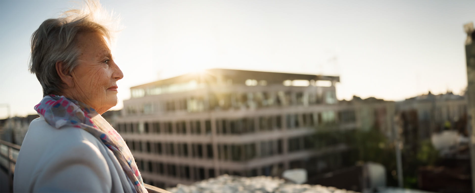 Une dame âgée bénéficie de sa pension complémentaire et regarde les appartements depuis son balcon.
