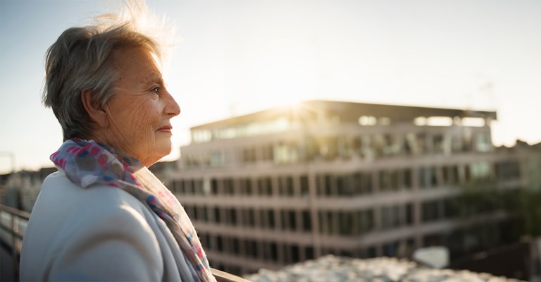 Oudere dame geniet van haar aanvullend pensioen en kijkt naar appartementen vanop haar balkon.