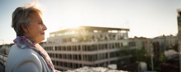 Oudere dame geniet van haar aanvullend pensioen en kijkt naar appartementen vanop haar balkon.