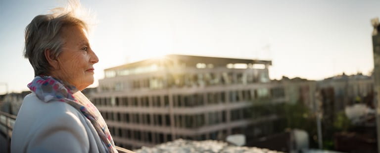 Oudere dame geniet van haar aanvullend pensioen en kijkt naar appartementen vanop haar balkon.