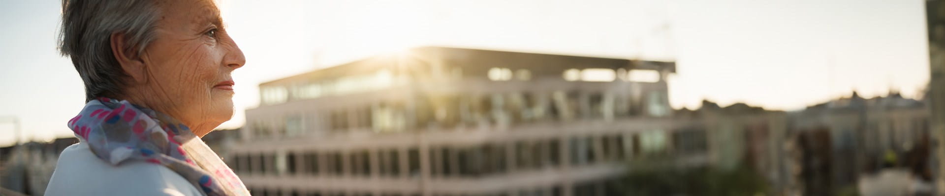 Oudere dame geniet van haar aanvullend pensioen en kijkt naar appartementen vanop haar balkon.