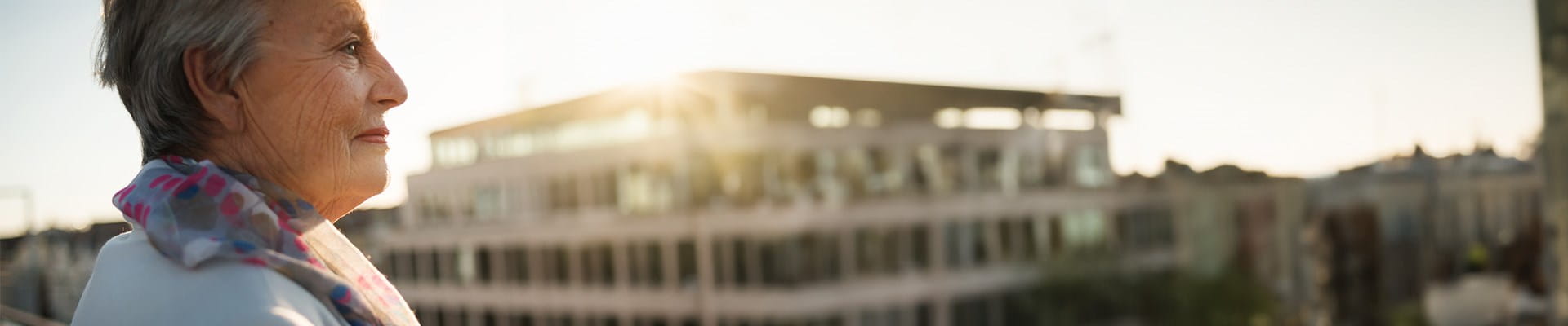Oudere dame geniet van haar aanvullend pensioen en kijkt naar appartementen vanop haar balkon.