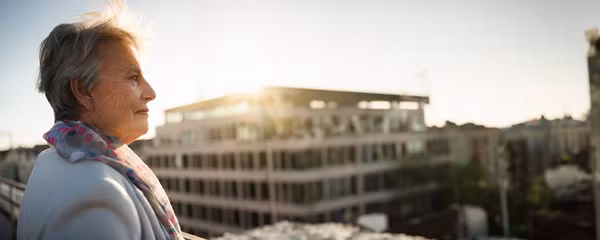 Une dame âgée bénéficie de sa pension complémentaire et regarde les appartements depuis son balcon.