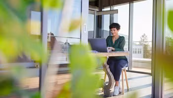 Une femme d'affaires souriante, assise à une table chez elle, travaillant sur son ordinateur portable.