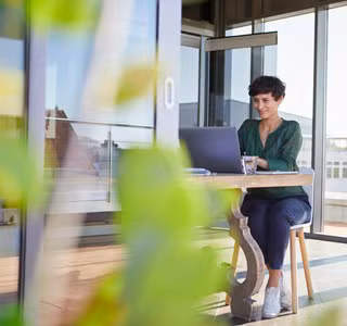Une femme d'affaires souriante, assise à une table chez elle, travaillant sur son ordinateur portable.